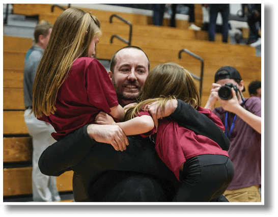 A man is holding three young girls in a stadium. AI generated content