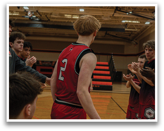 A group of people are on a basketball court, with one man wearing a red jersey and pointing at another player. AI generated content