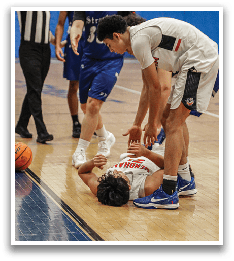 Two basketball players are on the court, one of them is kneeling down and the other is bending over him. The players are wearing blue and white uniforms. AI generated content