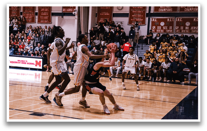 A basketball game is in progress with players on the court. A man is attempting to block a shot, while another player is trying to get the ball. The crowd watches intently from the stands. AI generated content