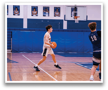 A basketball game is taking place in a gym with players on the court. One player is holding a basketball while another player is attempting to block him. There are other players on the court as well, some of whom are wearing blue and white uniforms. AI generated content
