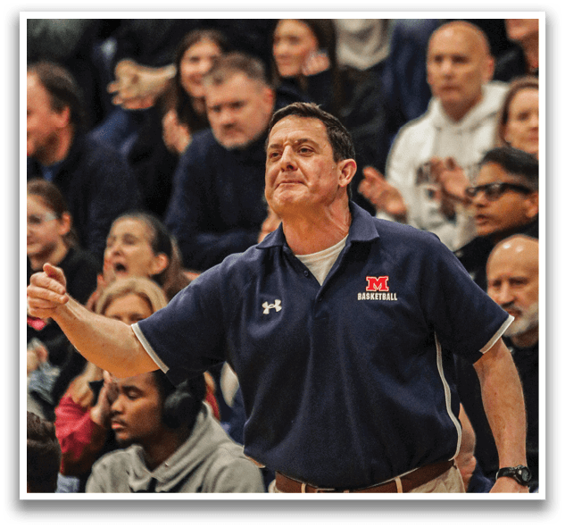 A man wearing a blue shirt and tan pants stands on a basketball court, waving his arms. He is surrounded by a crowd of people, some of whom are also wearing blue shirts. The man appears to be a coach or an important figure in the game. AI generated content