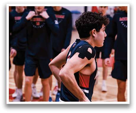 A group of young men are playing basketball on a court. One of the players is wearing a red and black jersey and has a brace on his arm. AI generated content