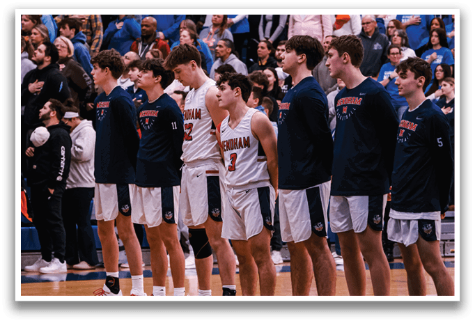 A group of young men wearing blue shirts and white shorts stand on a basketball court. They are lined up in front of a crowd of spectators. AI generated content