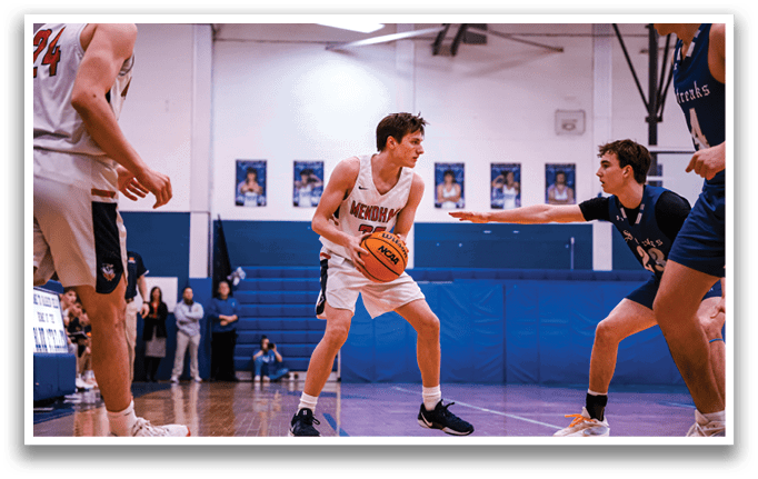 A basketball game is taking place with players on the court. One player is holding a basketball while another player is trying to block him. There are several other players on the court, some of them wearing blue uniforms. A bench can be seen in the background. AI generated content