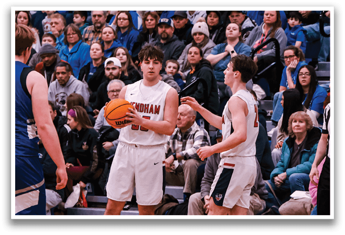 A basketball game is taking place with a crowd of people watching. A boy is holding a basketball, and a referee is standing nearby. The players are wearing blue and white uniforms. AI generated content