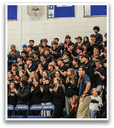 A crowd of people are sitting in the bleachers, watching a game. Some of the spectators are holding their hands up, cheering for the players. The crowd is diverse, with people of different ages and genders. A man in a blue shirt is standing near the crowd, possibly a coach or an official. The atmosphere is lively and energetic, as the spectators are fully engaged in the game. AI generated content