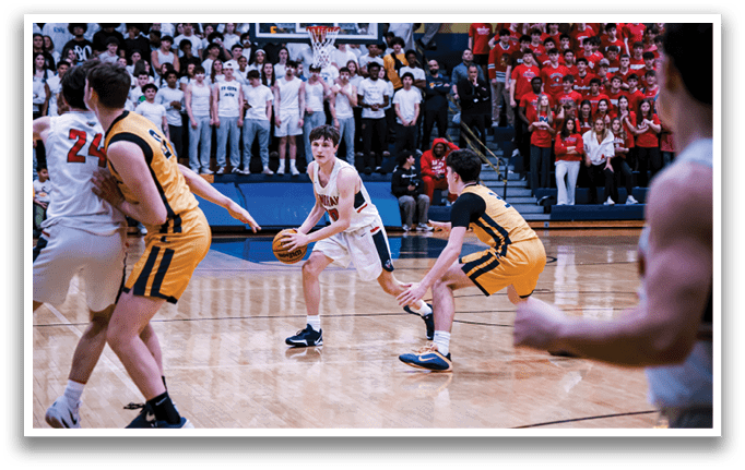 A basketball game is taking place with a group of people on the court. One player is holding a basketball while another player is trying to block him. The crowd is watching the game intently. AI generated content