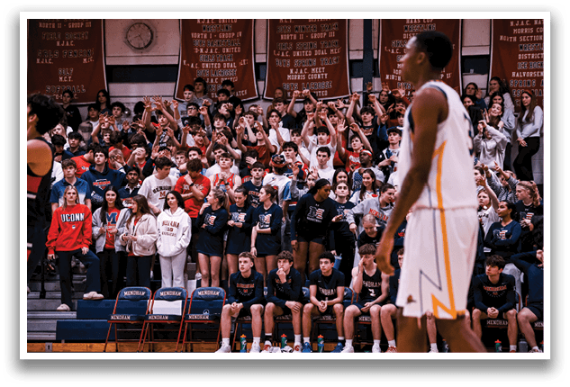 A basketball game is taking place with a crowd of people watching. A man is holding a basketball in his hand, and a clock is visible in the background. The spectators are seated on chairs, and some are standing. The atmosphere is lively, and the players are actively engaged in the game. AI generated content
