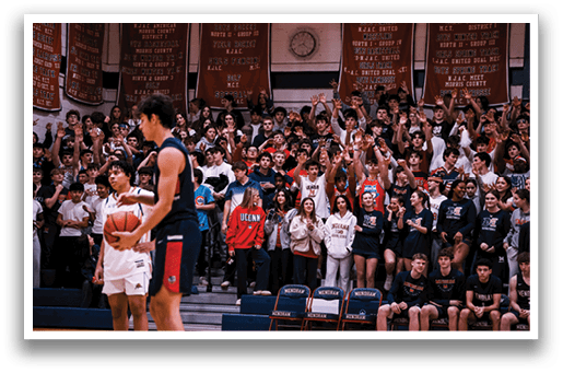 A basketball game is being played in front of a crowd of people. A man is holding a basketball, and a woman is holding a cell phone. The crowd is cheering and clapping, and there are chairs and a clock in the background. AI generated content