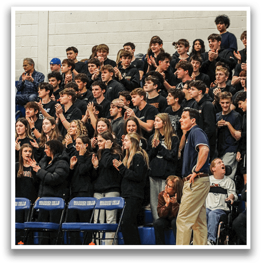 A crowd of people is standing in a gym, with some sitting on chairs. A man is standing in front of the crowd, possibly giving a speech or leading a group activity. The people are engaged and focused on the man, showing their interest in the event. AI generated content