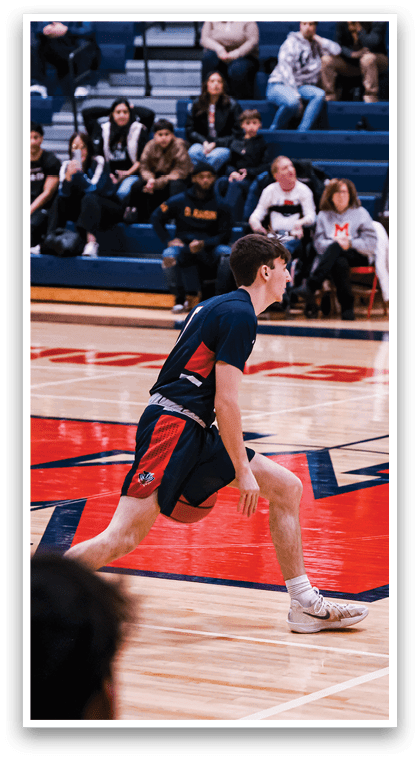 A basketball game is in progress with players on the court. One player is running with the ball while others are watching. The crowd is watching the game from the bleachers. AI generated content