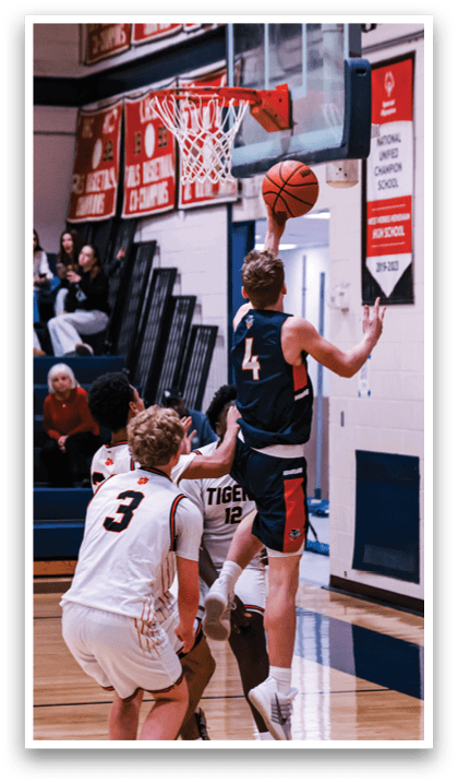A basketball player is jumping to block a shot, while another player is trying to get past him. The scene takes place in a gym with a crowd of people watching. AI generated content