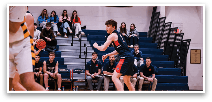 A basketball game is in progress with players on the court. A boy is running with a basketball, while other players are watching from the sidelines. There are several benches and chairs in the background, likely for spectators. AI generated content