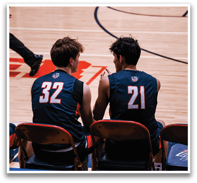 Two men wearing basketball uniforms sit on chairs on a basketball court. AI generated content