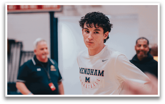 A man wearing a white shirt with the word “Mendham" on it stands on a basketball court. AI generated content