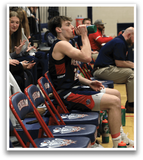 A group of people are sitting on chairs in a gym, watching a game. A man is drinking water from a bottle. AI generated content