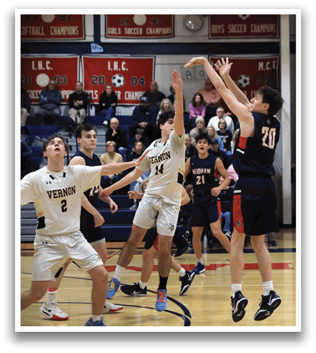 A basketball game is in progress with players from both teams trying to gain possession of the ball. The players are wearing uniforms and are actively engaged in the game. The basketball is in the air, and one player is attempting to block the shot. The game is being watched by a crowd of spectators who are seated on chairs surrounding the court. AI generated content
