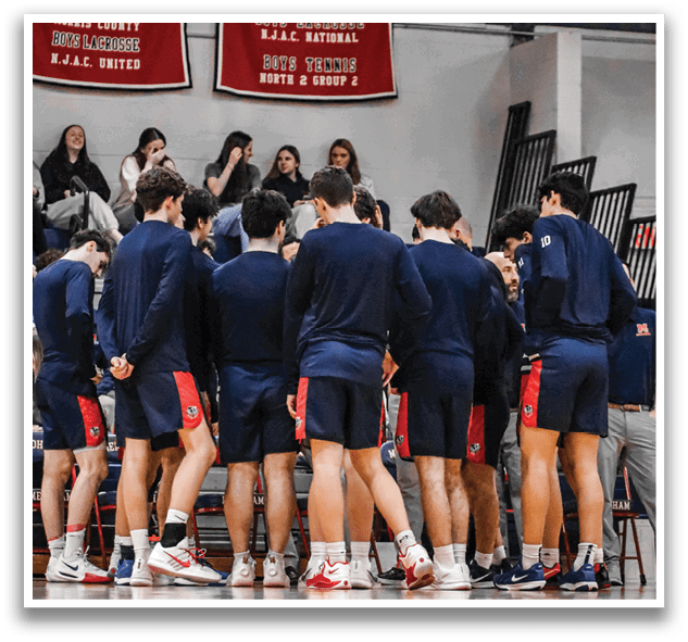 A group of young men wearing blue and red uniforms are standing in a circle on a basketball court. They are all looking down at the ground, possibly discussing their game strategy or listening to their coach. AI generated content