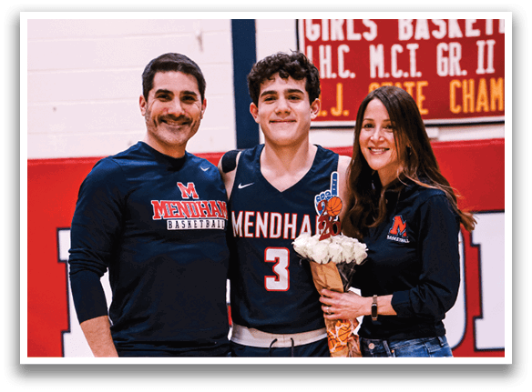A man, woman, and boy pose for a photo in front of a basketball court. The boy is holding a bouquet of flowers. AI generated content