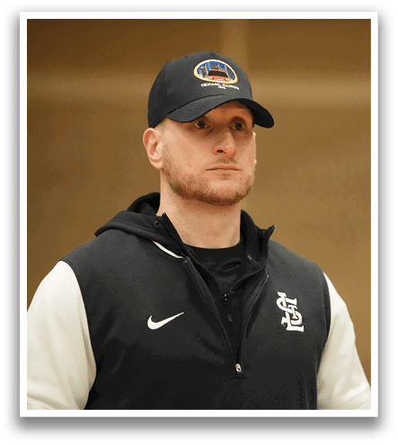 A man wearing a black hat and a black and white jacket stands in a gym. Contenido generado con IA