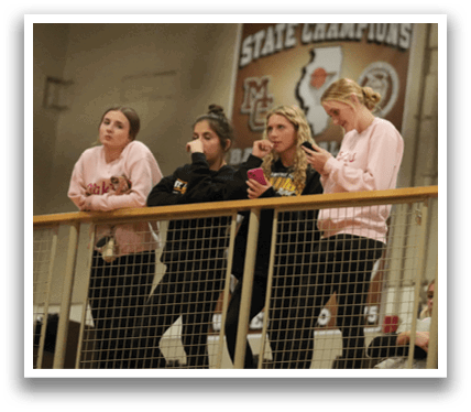 A group of people are standing on a balcony, watching a game. They are holding cell phones and drinking from cups. Contenido generado con IA