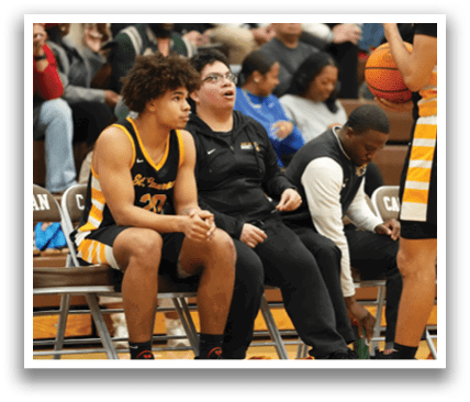 A group of people are sitting on chairs in a gym. One man is sitting on a chair with a basketball in his hand. Contenido generado con IA
