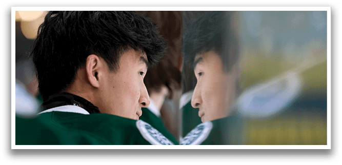A man with dark hair and a green shirt is looking at his reflection in a mirror. AI generated content