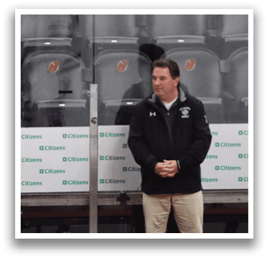 Three men are standing on a hockey rink, wearing their uniforms. They are positioned in front of a fence, likely waiting for their turn to play or observing the game. AI generated content