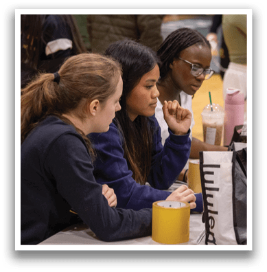 Three women are sitting around a table, looking at a laptop. One of them is holding a cup. AI generated content