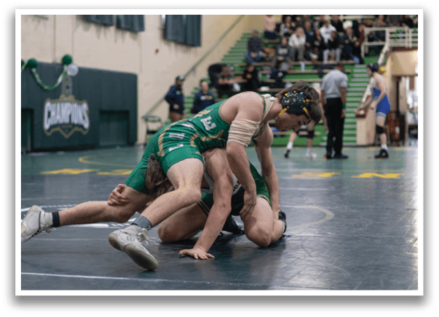 Two men are wrestling on a court, one in a green uniform and the other in a white uniform. They are both wearing headgear. The wrestling match is taking place in a gymnasium with a crowd of people watching. AI generated content