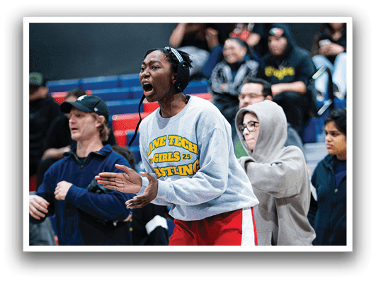 A group of people are watching a basketball game. A woman is standing up, holding her hands up, and appears to be yelling. A man is sitting down, also watching the game. There are several other people in the scene, some standing and some sitting, all focused on the game. AI generated content