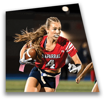 A person in football gear and helmet is crouched on a field with other players lined up in the background during a game. Description generated by AI