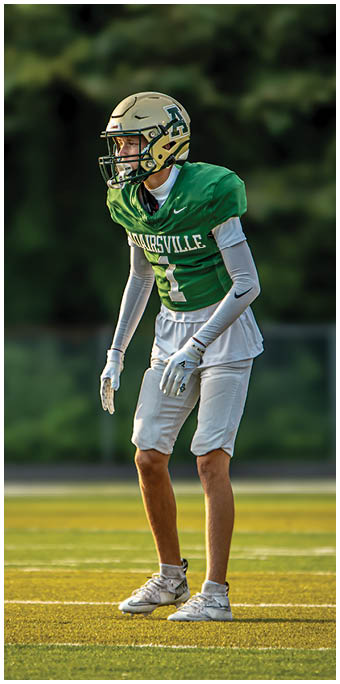Two people in football uniforms are engaged in a blocking action on a grassy field during a game or practice. Description generated by AI