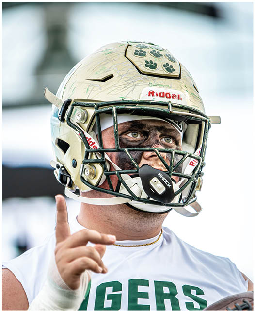 A person wearing a football helmet with face paint is raising one finger while looking upward. Description generated by AI