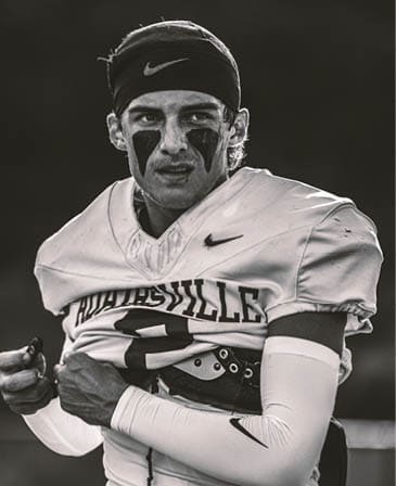 A person wearing a football uniform with the number 20 and a headband stands on a field with other players blurred in the background. Description generated by AI