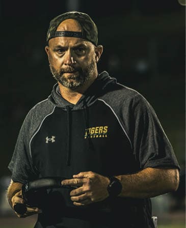 A person wearing a football helmet and jersey is closely listening to another person who is speaking and gesturing with their hand. Description generated by AI