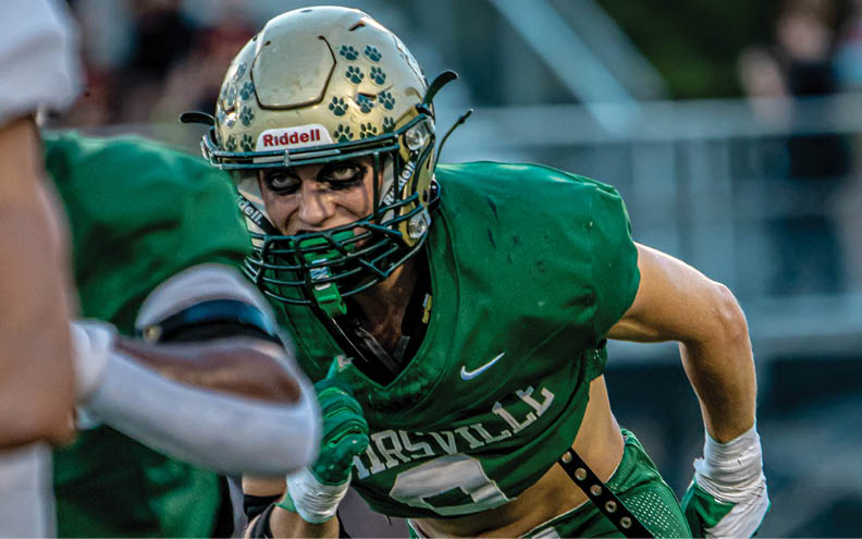 A person in green football gear and helmet is running on a field during a game. Description generated by AI