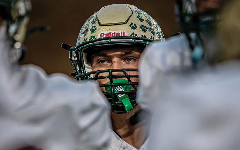 A person wearing a football helmet with paw prints is focused between two other players in white uniforms. Description generated by AI