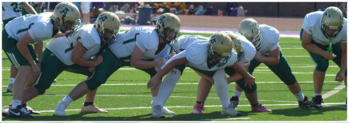 A group of people in football uniforms are lined up on a field in a ready stance, preparing for a play during a game or practice. Description generated by AI