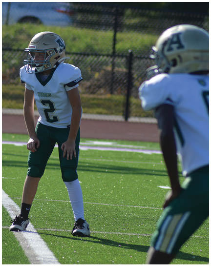 A person wearing a football uniform with the number 2 stands on a green field in a ready position during a game. Description generated by AI
