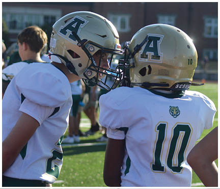 Two people wearing sports jerseys with numbers 21 and 10 stand side by side on a grassy field. Description generated by AI