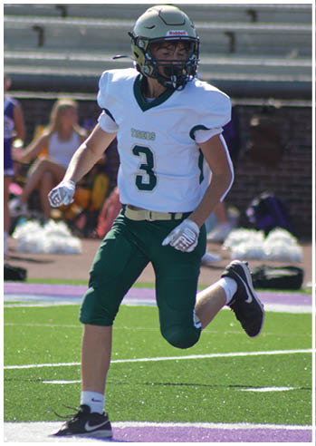 A person wearing a football uniform with the number three is running on a green field near a purple sideline. Description generated by AI