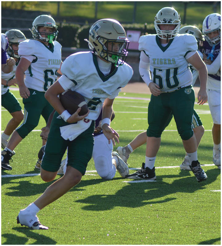 A group of young athletes in football uniforms are playing on a sunlit field with one player running while holding the ball. Description generated by AI
