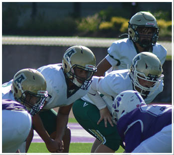 Several people wearing football helmets and uniforms are positioned closely together on a field, appearing ready for a play. Description generated by AI