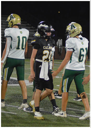 Four people wearing football uniforms are standing on a field at night, with three in white and green uniforms and one in a black uniform. Description generated by AI