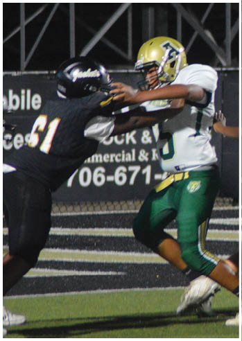 Two people in football uniforms are engaged in a play on a field, with one person in a white and green uniform blocking another in a black uniform. Description generated by AI