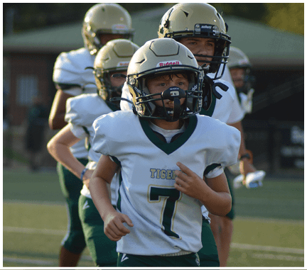 Children wearing football helmets and uniforms are running on a sports field during a game or practice. Description generated by AI