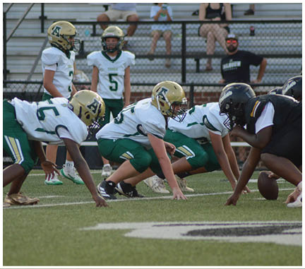 People in football uniforms are crouched in a ready position on a grassy field, preparing for a play. Description generated by AI