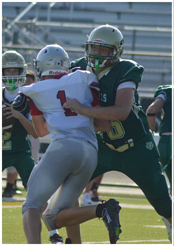 Two people in football uniforms are engaged in a tackle on a field with empty bleachers in the background. Description generated by AI